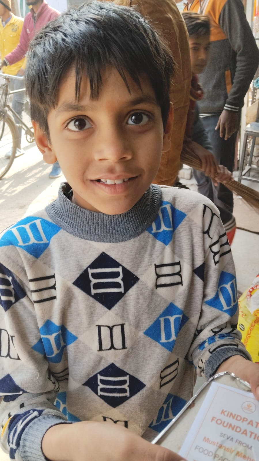 A smiling child holding a Kindpath Foundation food packet during a food seva distribution